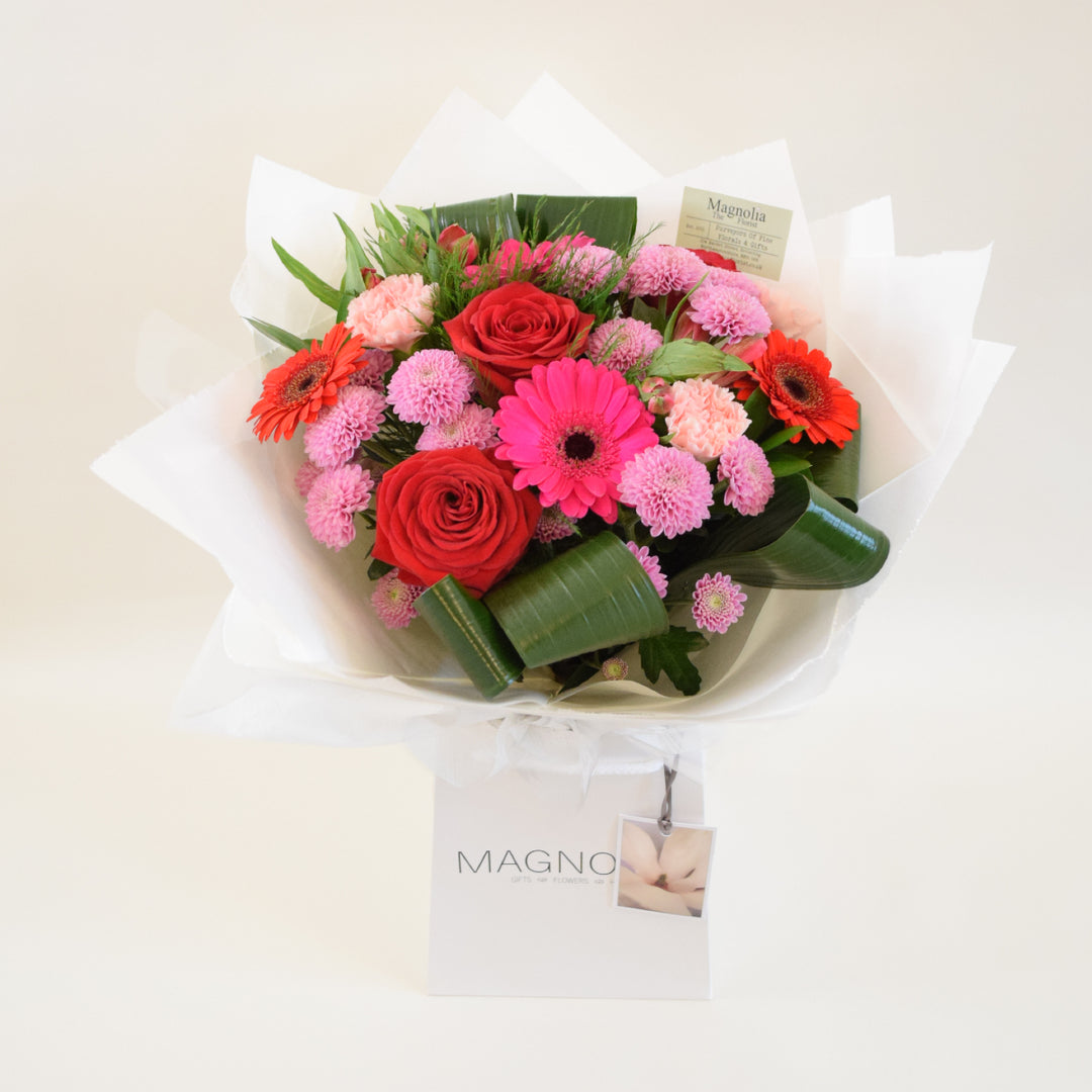 Buckingham Hand-Tied Bouquet - Magnolia the Florist Expertly crafted and arranged by hand, the Buckingham Hand-Tied Bouquet from Magnolia the Florist, features a stunning combination of red and pink-toned flowers, including roses, gerbera, alstroemeria, carnation, chrysanthemum, and foliage. Presented in our signature box bag, this aqua bouquet is sure to make a beautiful and thoughtful gift for any occasion.