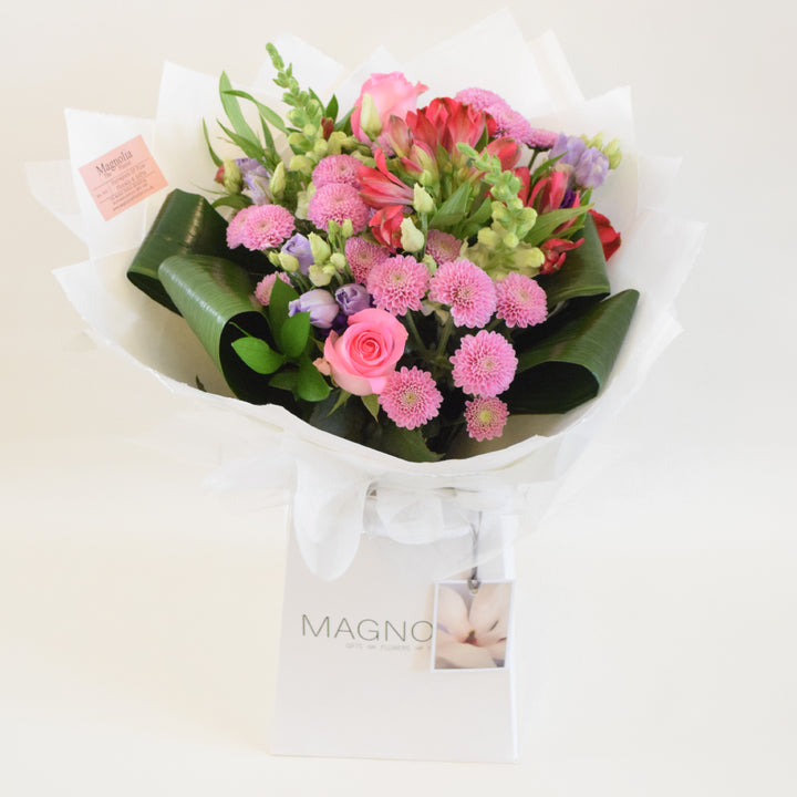 Chelsea Hand-Tied Bouquet - Magnolia the Florist Our Chelsea Bouquet from Magnolia the Florist, is a stunning combination of pink, white, and a hint of purple flowers, including roses, antirrhinum, lisanthus, alstromeria, and chrysanthemum. Presented in our signature box bags, it is perfect for any occasion.