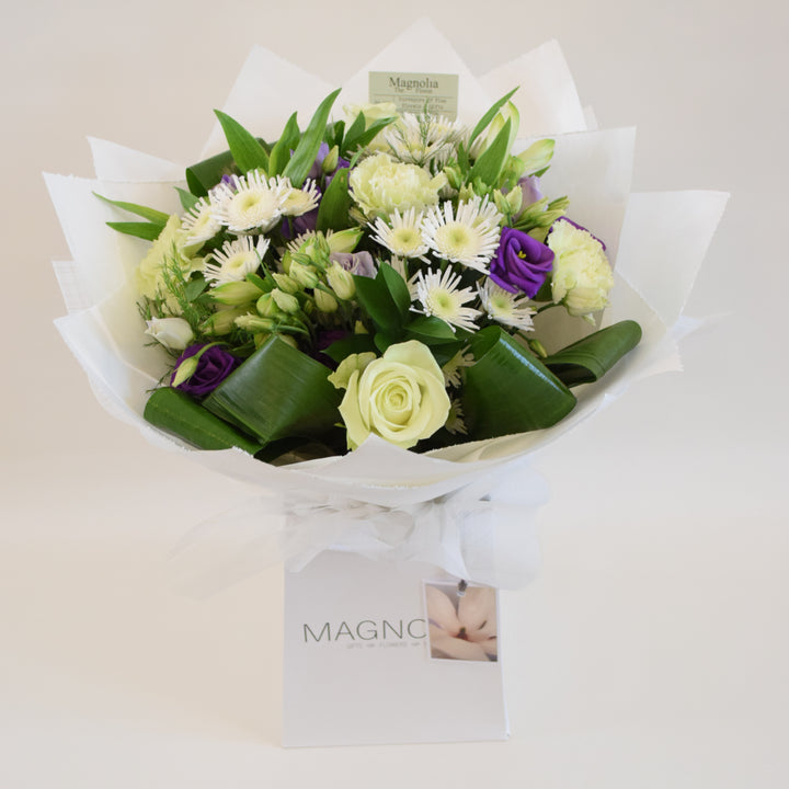 Clarence Hand-Tied Bouquet - Magnolia the Florist Indulge in the elegance and beauty of our Clarence Hand-Tied Bouquet from Magnolia the Florist. Featuring a stunning mix of white and purple tones, this hand-tied bouquet includes a variety of premium flowers including roses, lisianthus, carnations, alstroemeria, chrysanthemum and lush foliage. The perfect gift for someone special, presented in one of our signature hand-tied bags.