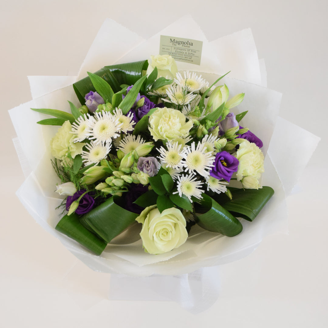 Clarence Hand-Tied Bouquet - Magnolia the Florist Indulge in the elegance and beauty of our Clarence Hand-Tied Bouquet from Magnolia the Florist. Featuring a stunning mix of white and purple tones, this hand-tied bouquet includes a variety of premium flowers including roses, lisianthus, carnations, alstroemeria, chrysanthemum and lush foliage. The perfect gift for someone special, presented in one of our signature hand-tied bags.