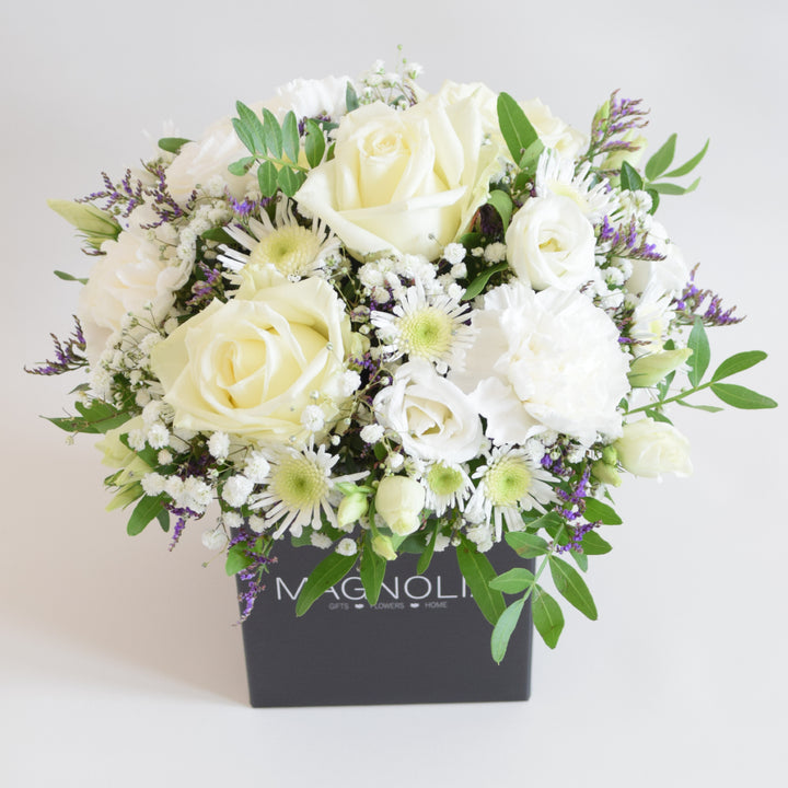 Dainty Kew Arrangement - Magnolia the Florist The Kew Arrangement from Magnolia the Florist, features a stunning mix of white florals with a hint of purple, including roses, carnations, lisianthus, gyp, chrysanthemum and limonium, all arranged in floral foam. Presented in a signature box, it makes a beautiful and sophisticated gift for any occasion. For scale purposes, the box container measures approximately 15cm x 12cm x 12cm, giving the overall arrangement size of 25cm h x 18cm w approximately.