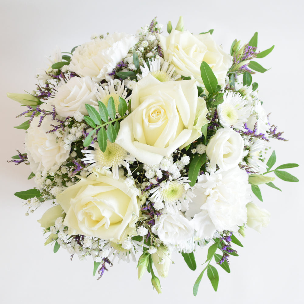 Dainty Kew Arrangement - Magnolia the Florist The Kew Arrangement from Magnolia the Florist, features a stunning mix of white florals with a hint of purple, including roses, carnations, lisianthus, gyp, chrysanthemum and limonium, all arranged in floral foam. Presented in a signature box, it makes a beautiful and sophisticated gift for any occasion. For scale purposes, the box container measures approximately 15cm x 12cm x 12cm, giving the overall arrangement size of 25cm h x 18cm w approximately.