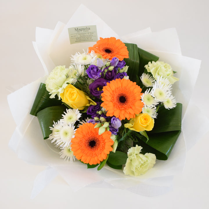 Savoy Hand-Tied Bouquet - Magnolia the Florist With vibrant hues of yellow, orange, green, and purple, the Savoy Hand-Tied Bouquet from Magnolia the Florist, is a stunning mix of Roses, Mini Gerbera, Lisianthus, Carnations, Chrysanthemums, and foliage. Expertly arranged in our signature box bags, this aqua bouquet is sure to brighten any space. Perfect for any occasion, bring a touch of nature's beauty into your home today.