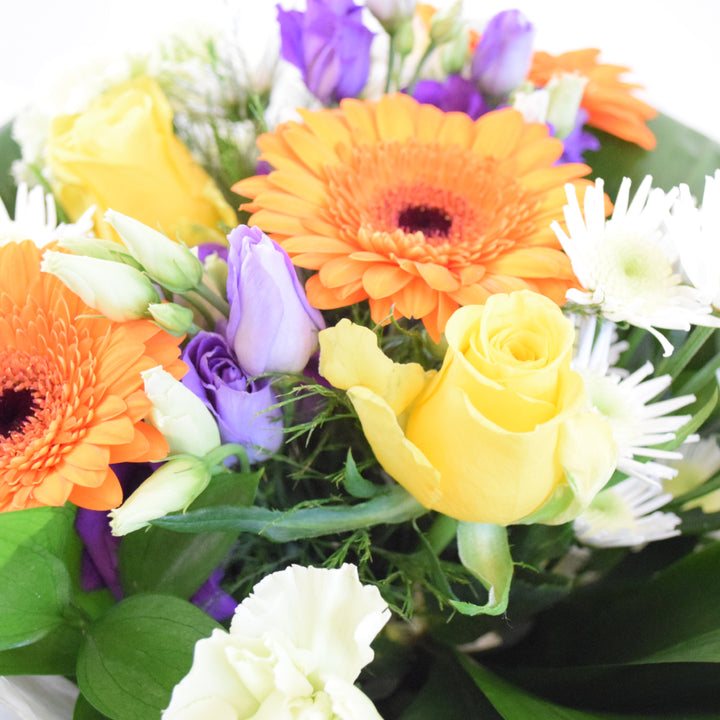 Savoy Hand-Tied Bouquet - Magnolia the Florist With vibrant hues of yellow, orange, green, and purple, the Savoy Hand-Tied Bouquet from Magnolia the Florist, is a stunning mix of Roses, Mini Gerbera, Lisianthus, Carnations, Chrysanthemums, and foliage. Expertly arranged in our signature box bags, this aqua bouquet is sure to brighten any space. Perfect for any occasion, bring a touch of nature's beauty into your home today.