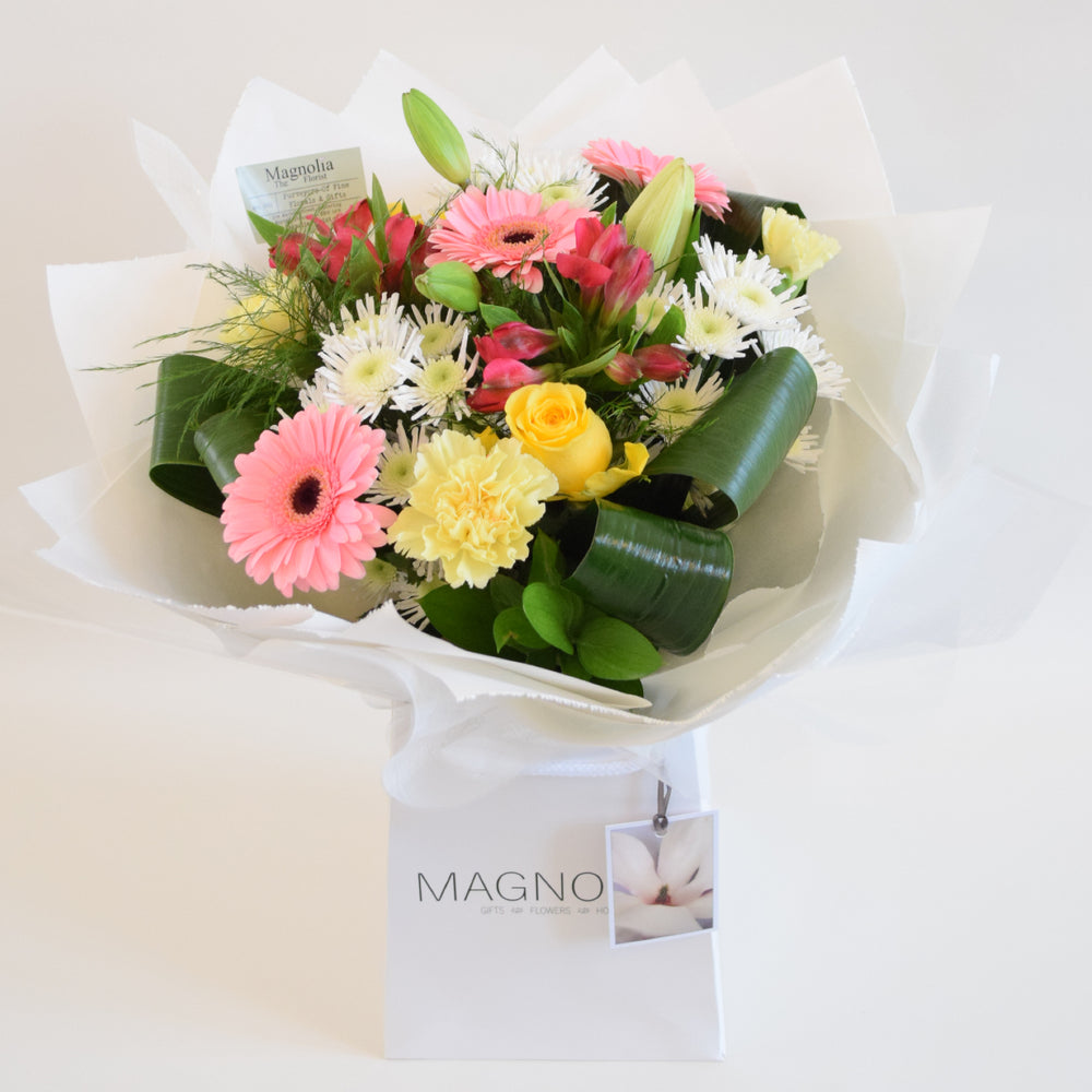 St James Hand-Tied Bouquet - Magnolia the Florist Indulge in luxury with the St James hand-tied bouquet from Magnolia the Florist. A stunning arrangement of lilies, roses, chrysanthemums, carnations, alstroemeria, and mini gerbera in white, yellow, and pink tones. Expertly hand-tied and presented in our elegant box bag, this bouquet is sure to impress.