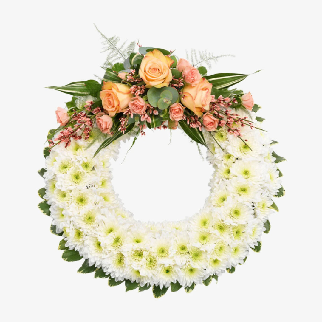 Based Wreath - Magnolia the Florist A classic circular wreath covered with a mass of white Double Spray Chrysanthemums and finished with a spray of coloured flowers. This image shows a selection of peach-toned flowers, the spray can be changed to other colour options. Please select from the options below. If you cannot find what you want on our site, please call our sales team, we're always happy to assist you. This item requires 3 days notice to order.